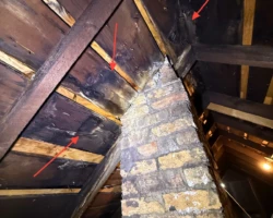Dark water staining on attic roof sheathing where a masonry chimney passes through